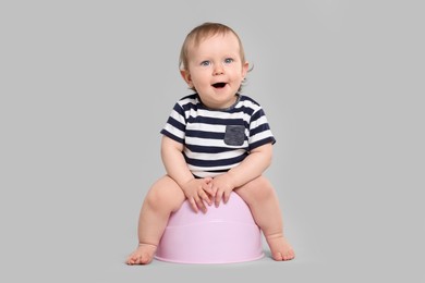 Photo of Little child sitting on baby potty against light grey background