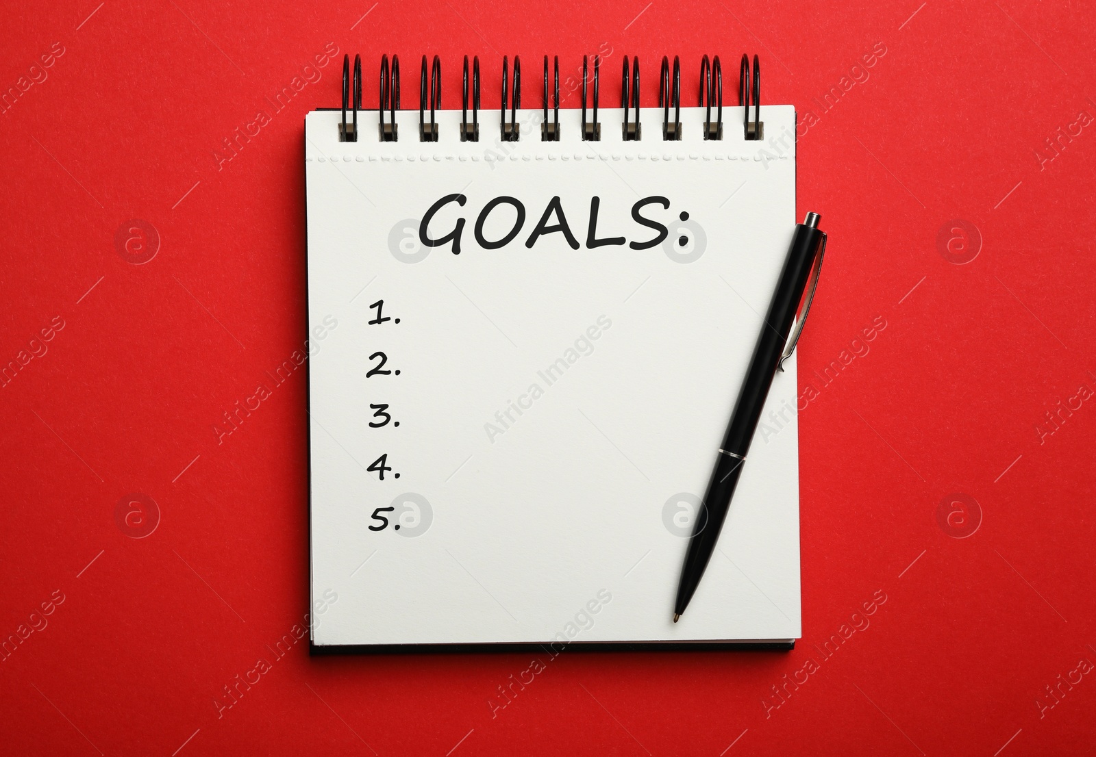 Image of Pen and notebook with inscription GOALS on red background, top view. New Year aims 