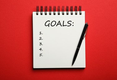 Pen and notebook with inscription GOALS on red background, top view. New Year aims 