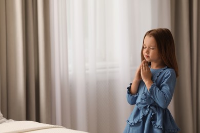 Photo of Cute little girl saying bedtime prayer at home. Space for text