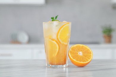 Tasty refreshing drink with orange on white marble table in kitchen