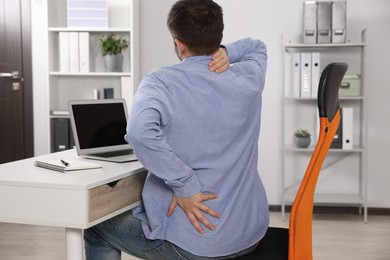 Photo of Man suffering from back pain while working with laptop in office. Symptom of scoliosis