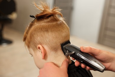 Professional hairdresser cutting boy's hair in beauty salon, closeup