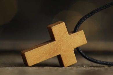 Photo of Christian cross on wooden table against blurred background, closeup