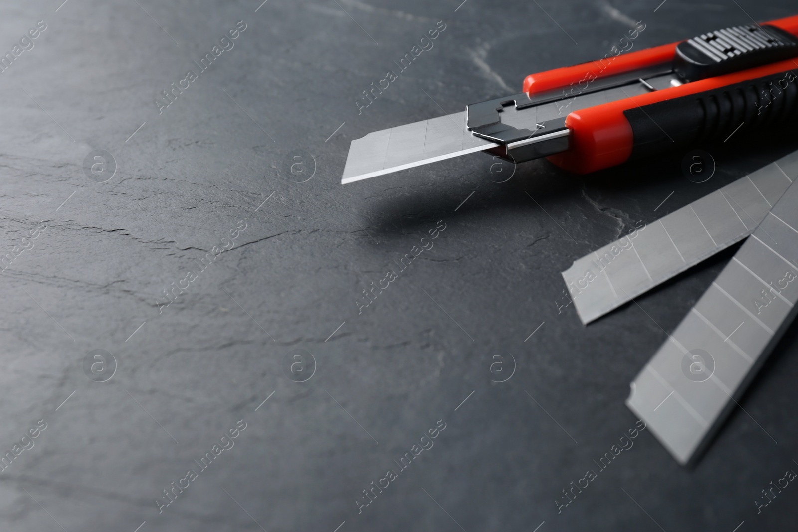 Photo of Utility knife and blades on black table. Space for text