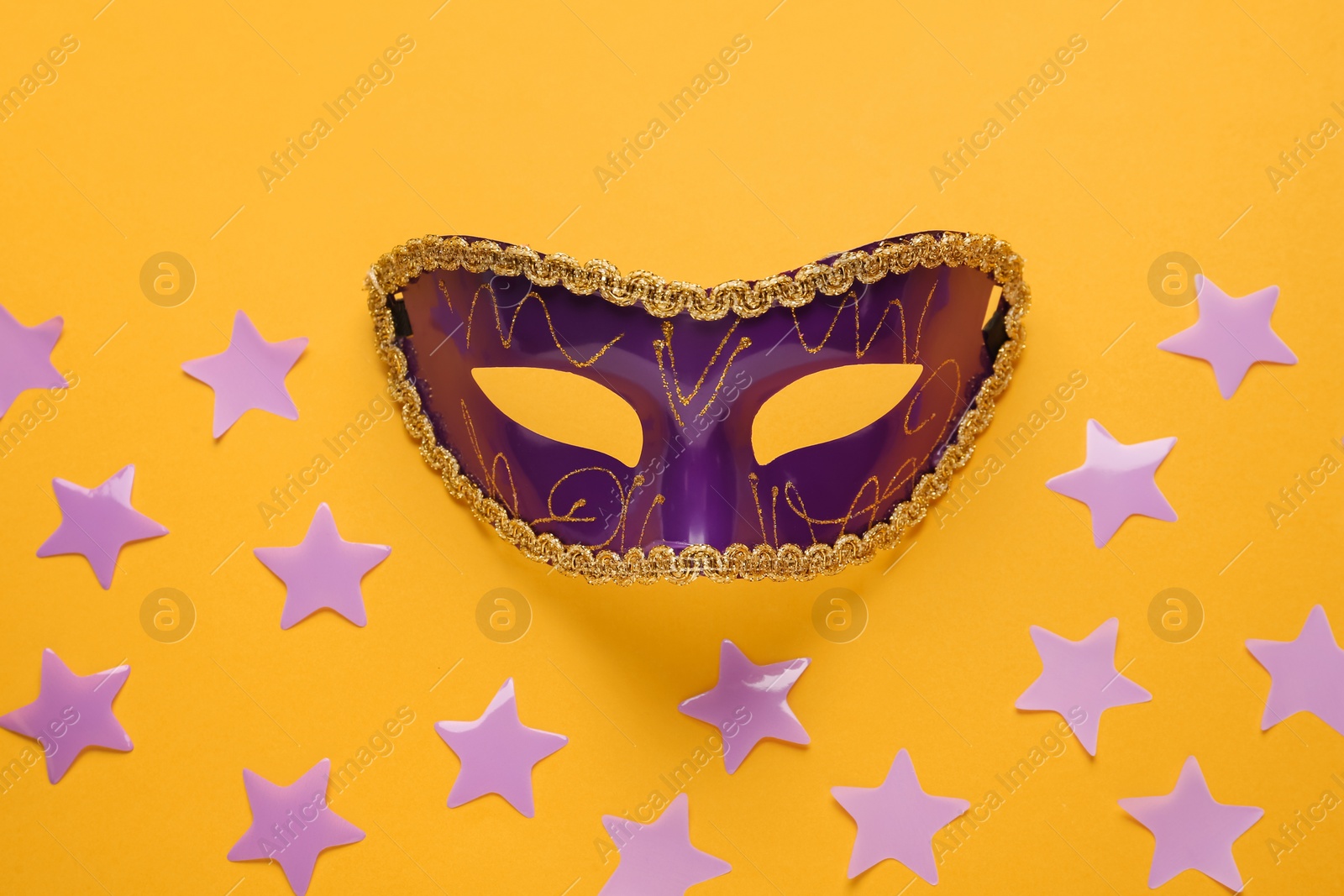 Photo of Beautiful purple carnival mask and confetti on orange background, top view