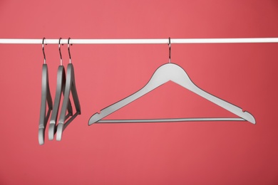 Empty clothes hangers on metal rail against color background