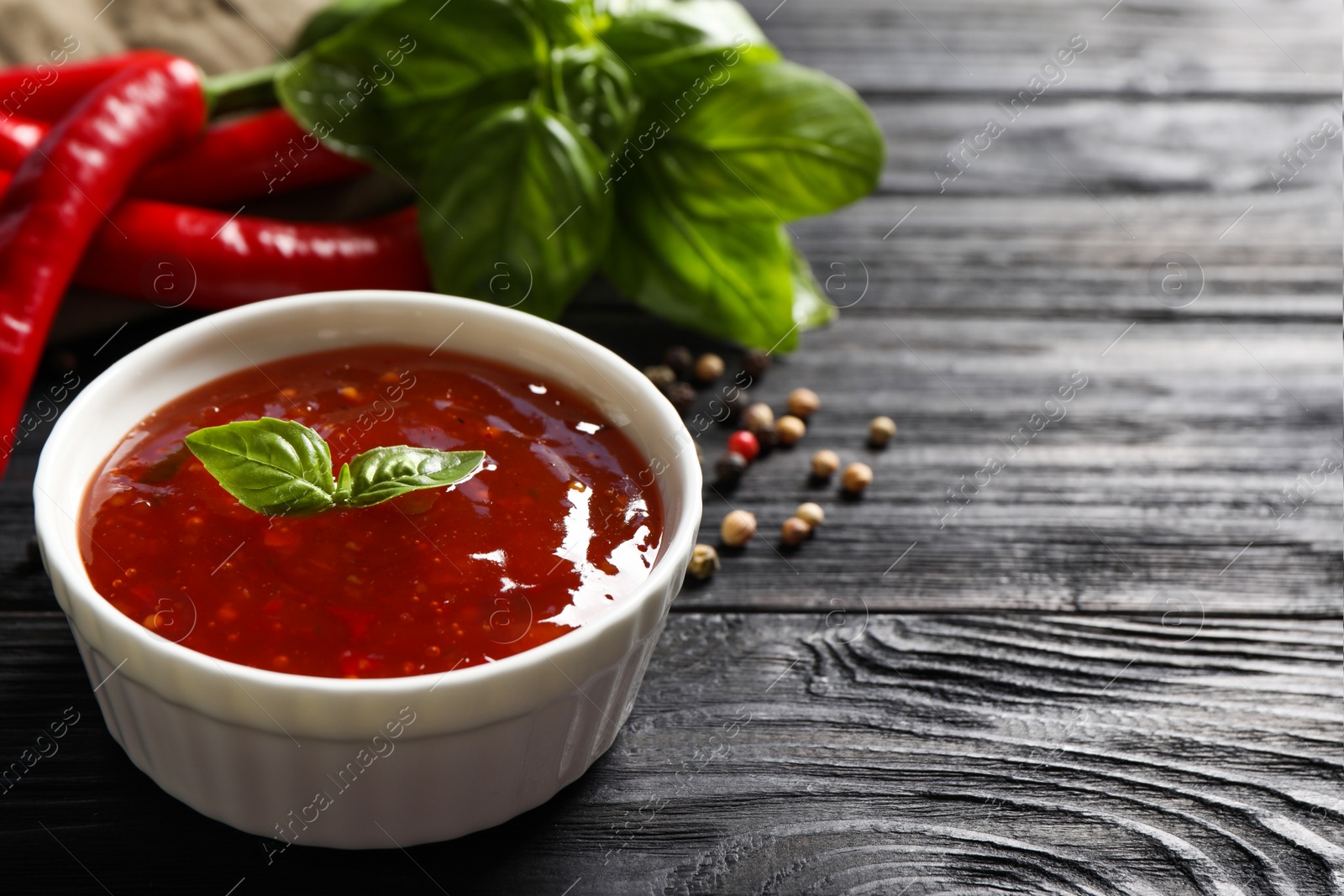 Photo of Spicy chili sauce with basil on dark wooden table, space for text