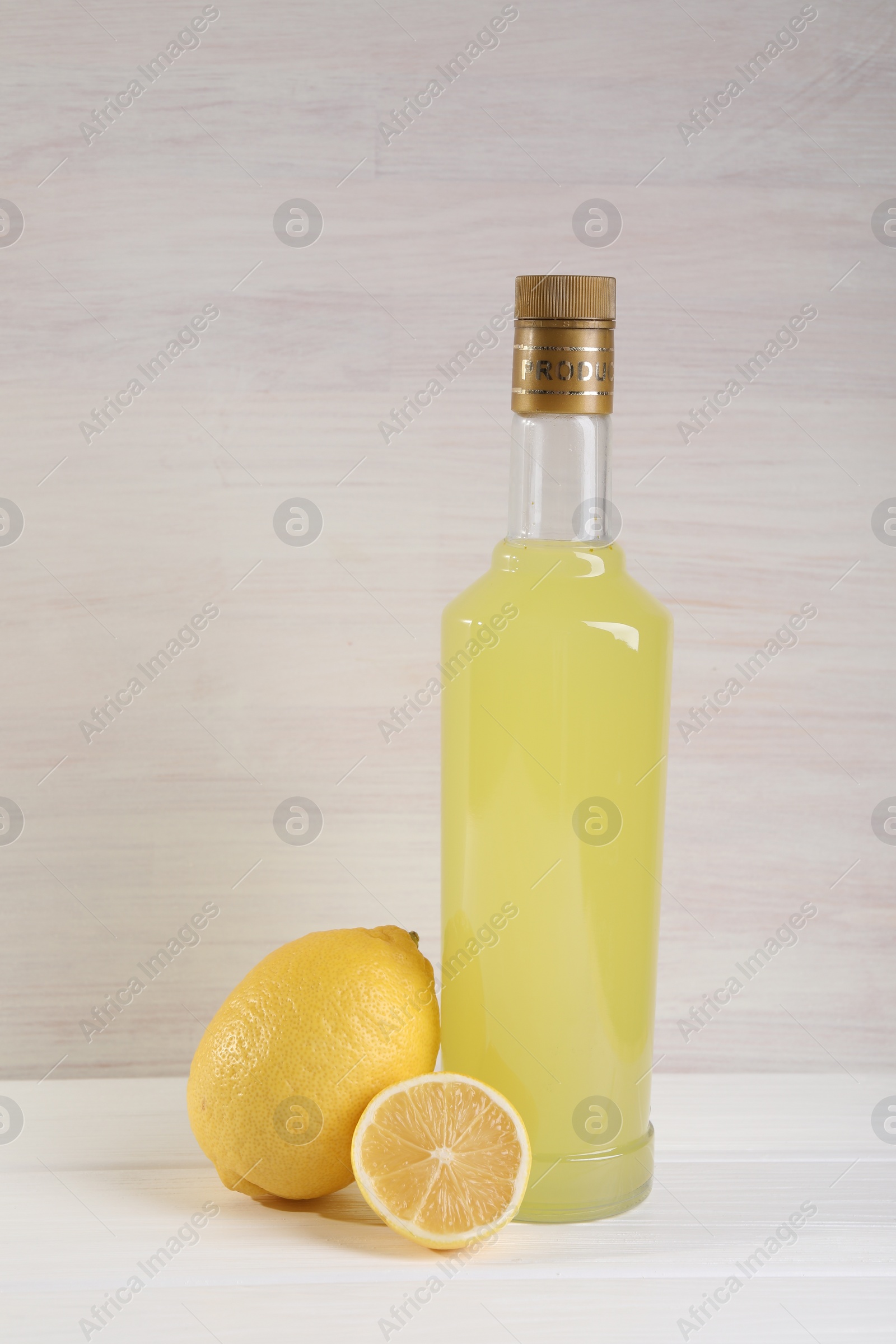 Photo of Bottle of tasty limoncello liqueur and lemons on white wooden table