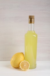 Photo of Bottle of tasty limoncello liqueur and lemons on white wooden table