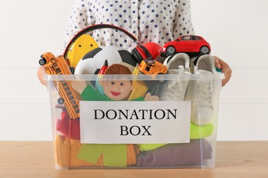 Photo of Woman holding donation box with child goods against light background, closeup