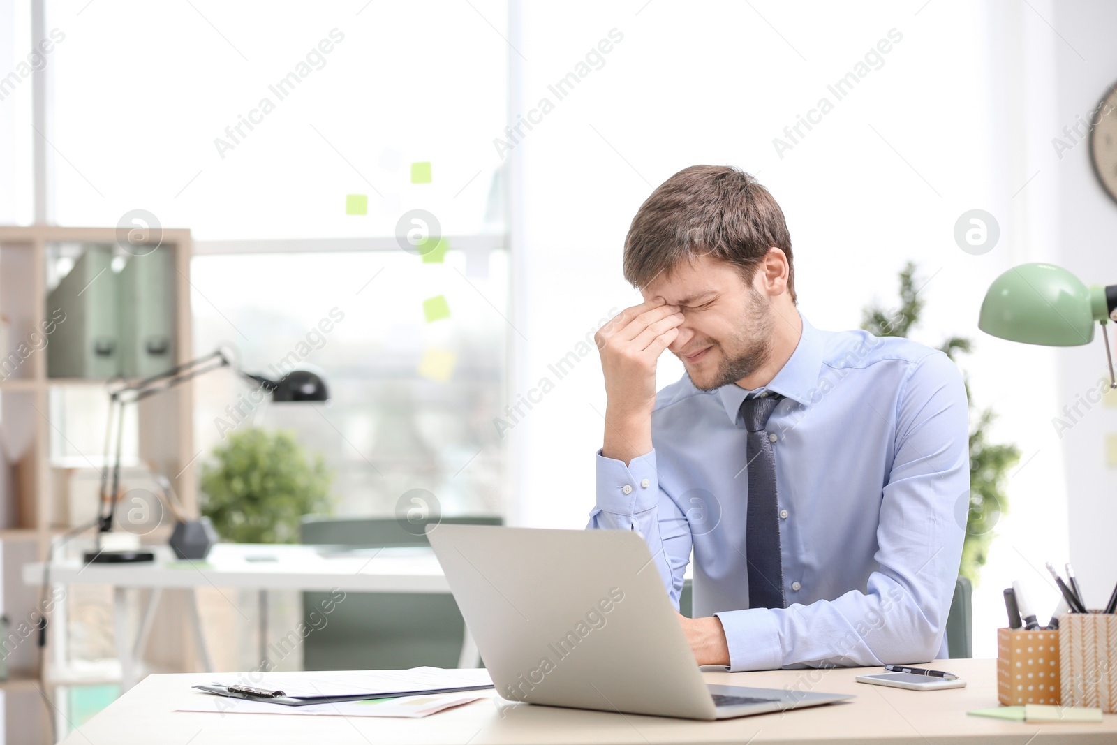 Photo of Young man suffering from headache in office