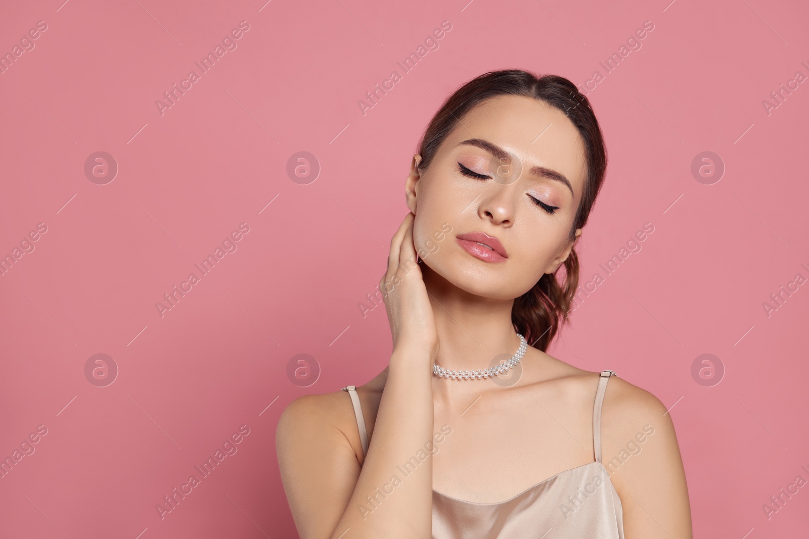 Photo of Young woman wearing elegant pearl necklace on pink background, space for text