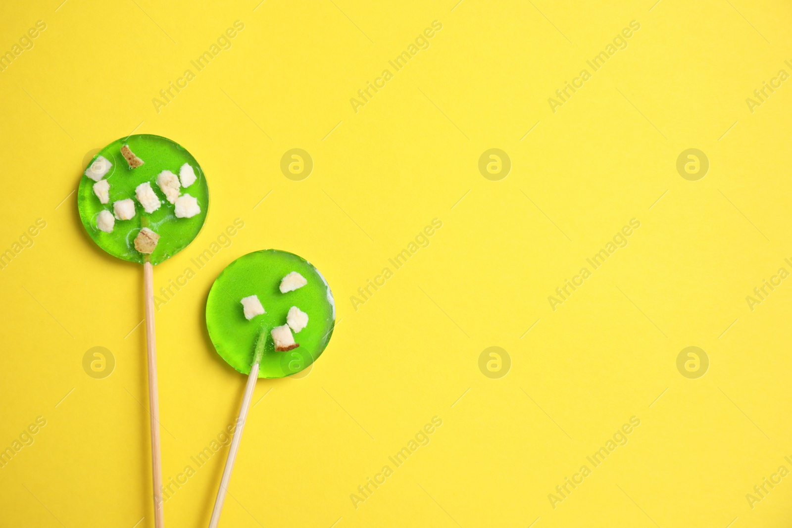 Photo of Sticks with light green lollipops on yellow background, flat lay. Space for text