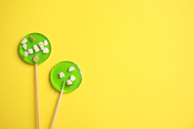 Photo of Sticks with light green lollipops on yellow background, flat lay. Space for text
