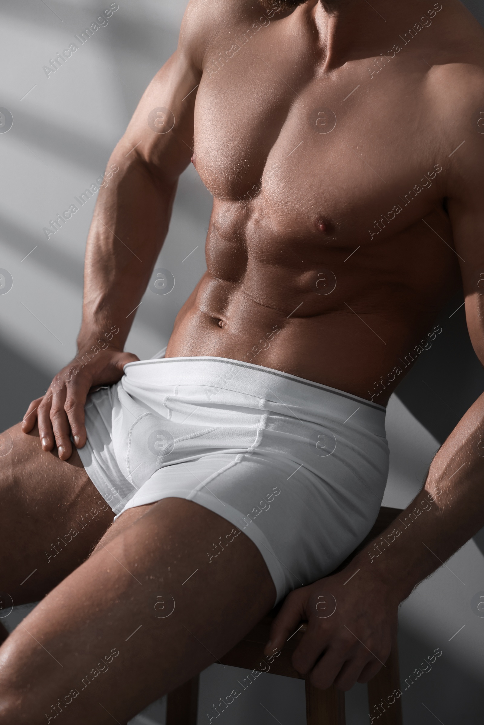 Photo of Young man in stylish white underwear sitting on chair near grey wall, closeup