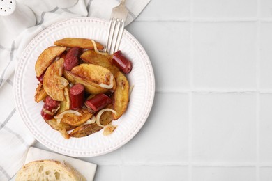 Photo of Delicious baked potato with thin dry smoked sausages and onion served on white tiled table, flat lay. Space for text