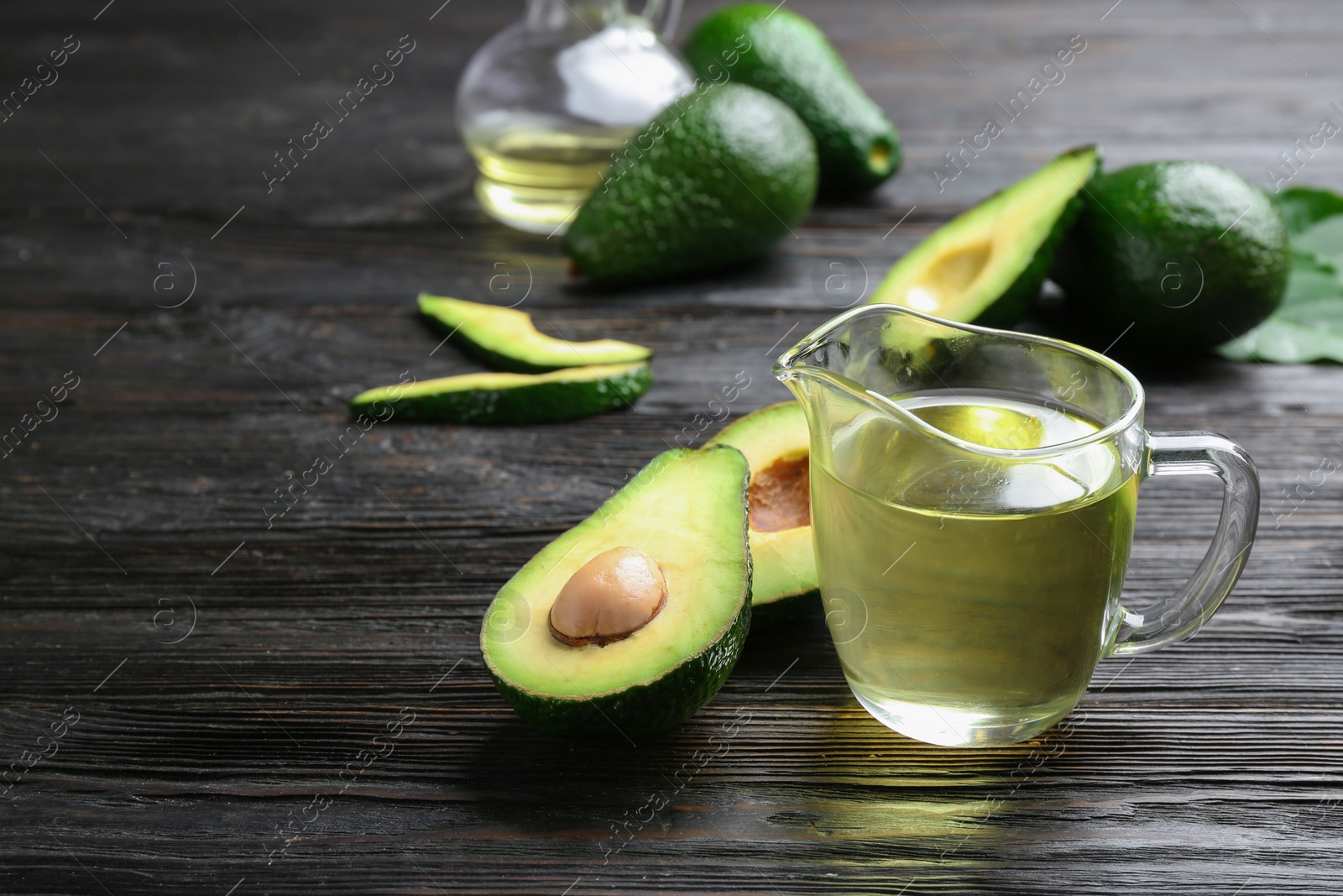 Photo of Jug of natural oil and avocados on dark wooden background. Space for text