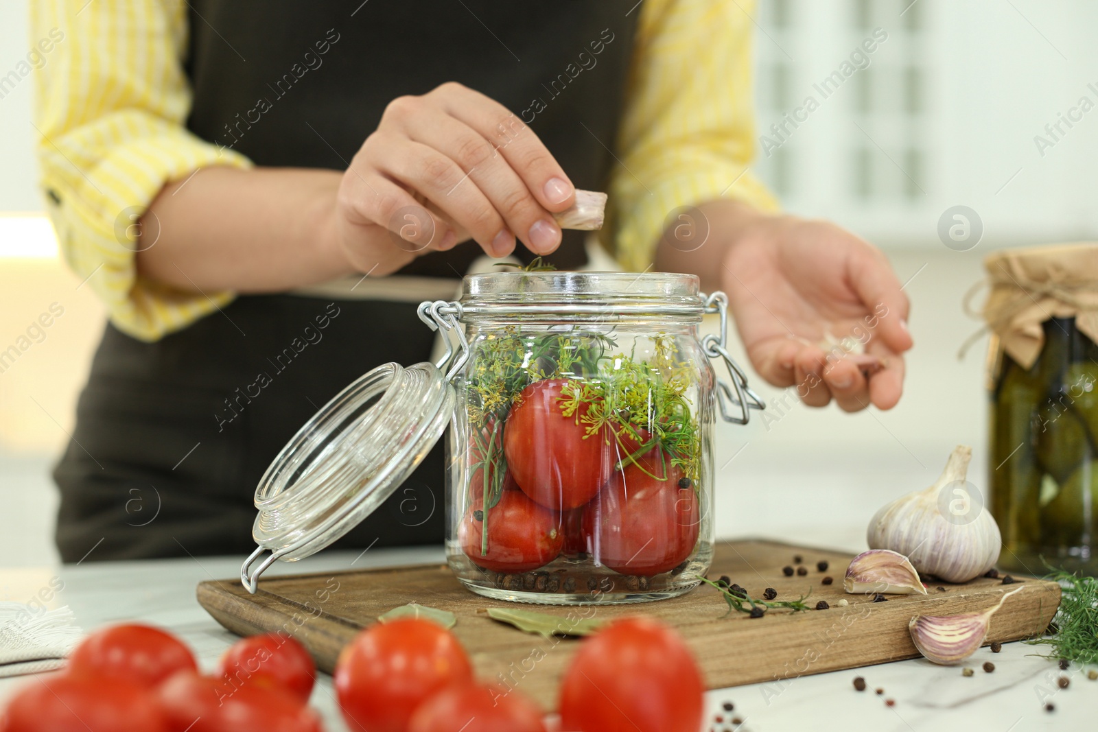 Photo of Woman putting garlic into pickling jar at table in kitchen, closeup