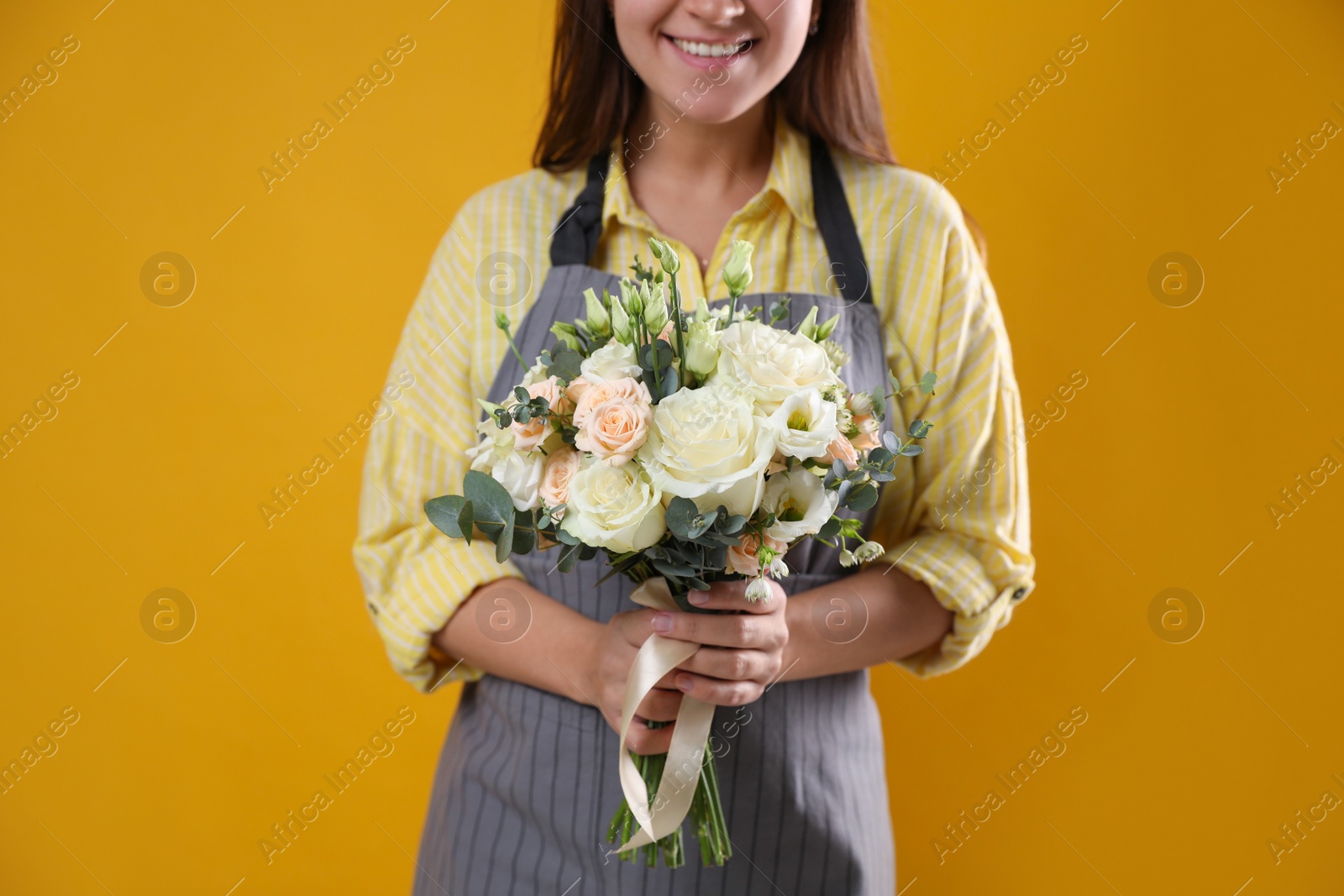 Photo of Florist holding beautiful wedding bouquet on yellow background, closeup