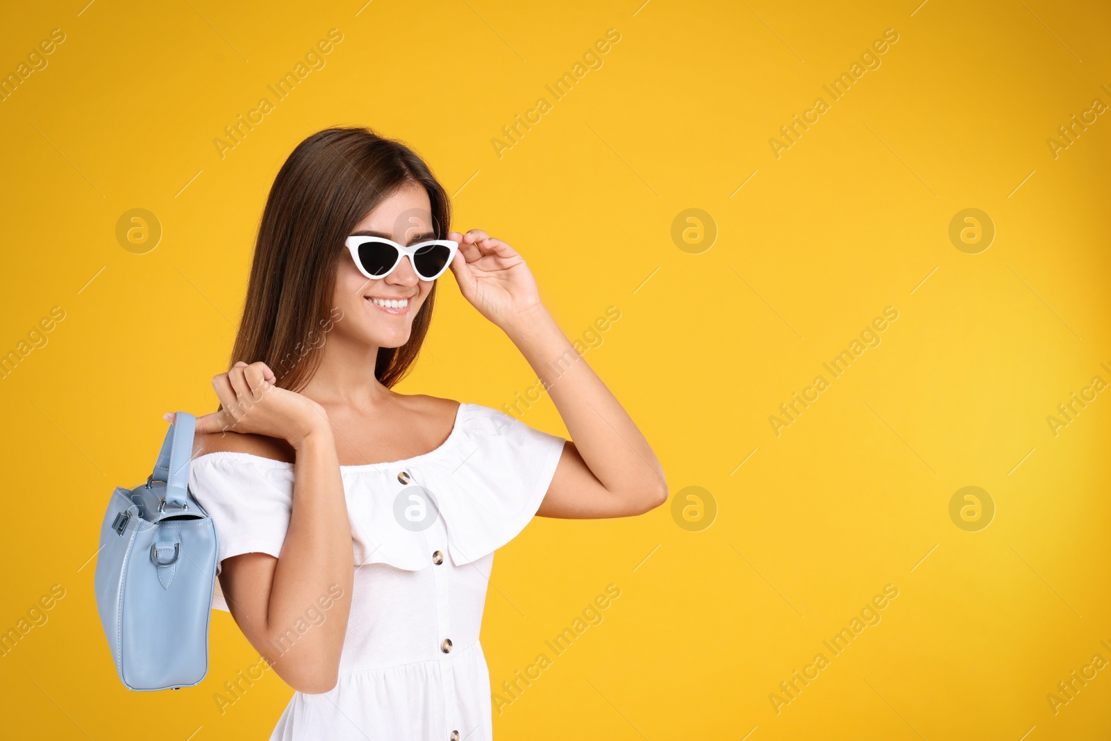 Photo of Young woman wearing stylish white dress with elegant bag on yellow background. Space for text