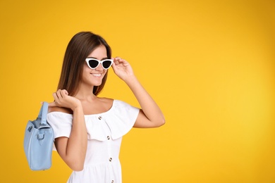 Young woman wearing stylish white dress with elegant bag on yellow background. Space for text