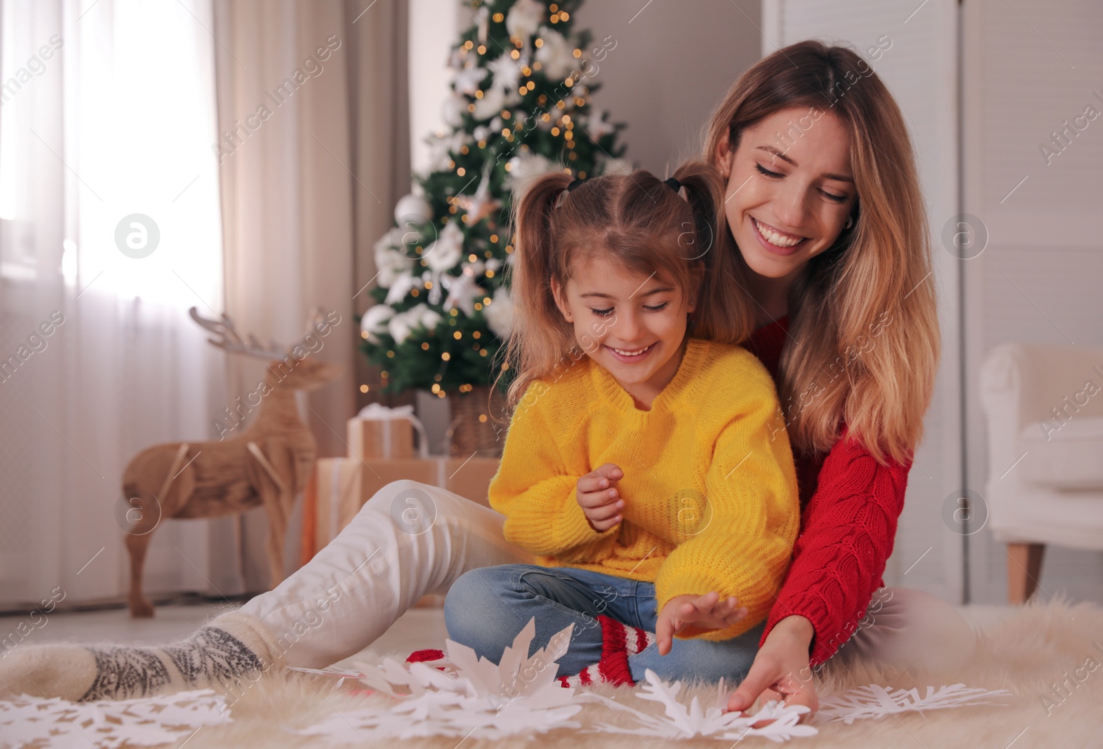 Photo of Happy mother and daughter making paper snowflakes near Christmas tree at home