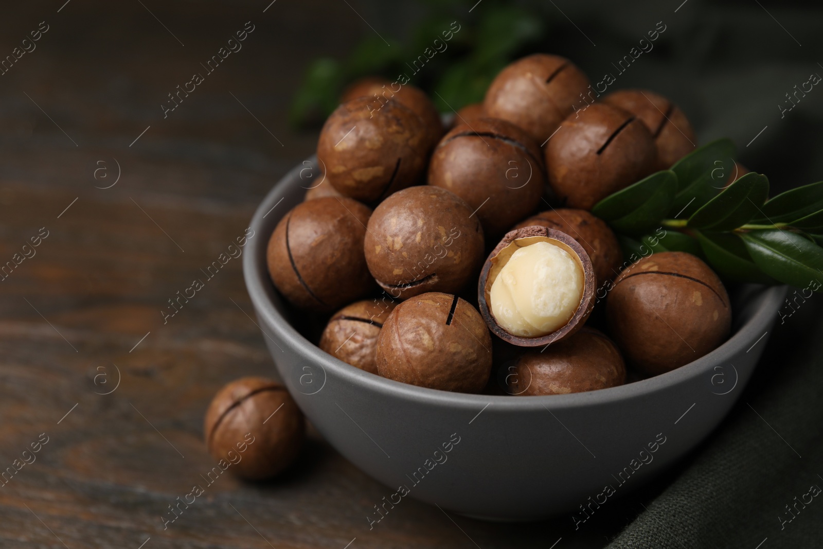 Photo of Tasty Macadamia nuts and green twig in bowl on wooden table, closeup. Space for text