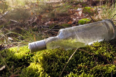 Used glass bottle on green grass outdoors. Recycling problem