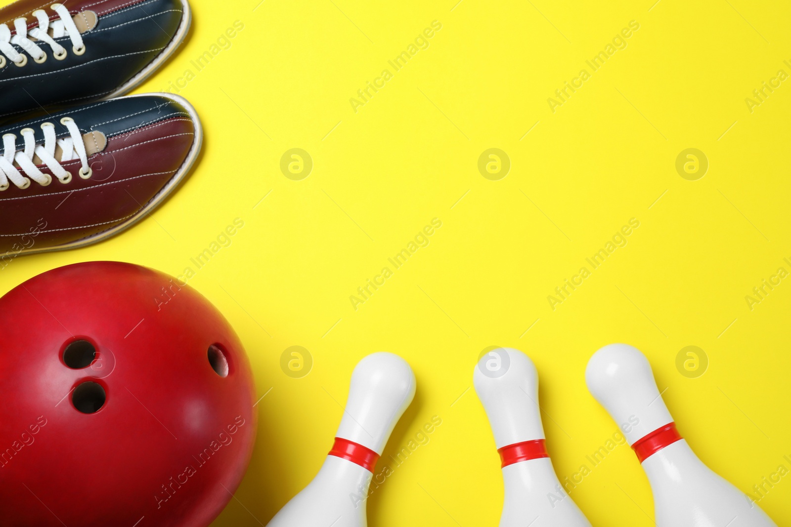 Photo of Bowling ball, shoes and pins on yellow background, flat lay. Space for text