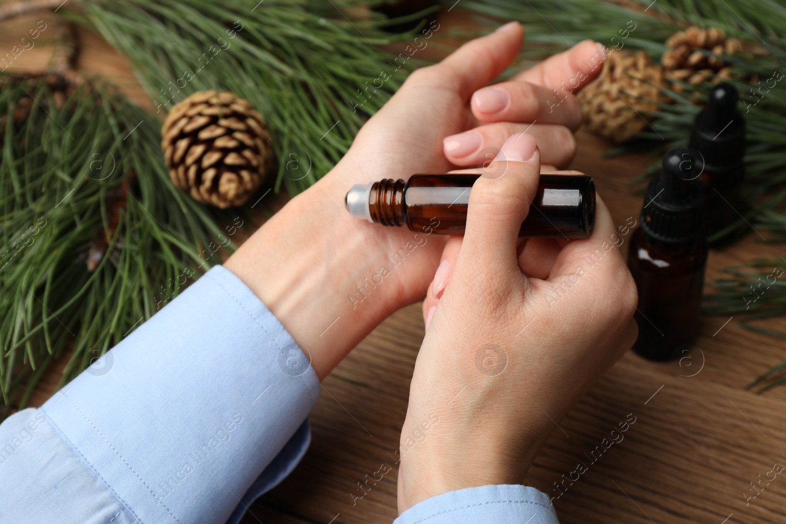 Photo of Woman applying pine essential oil on wrist at wooden table, closeup