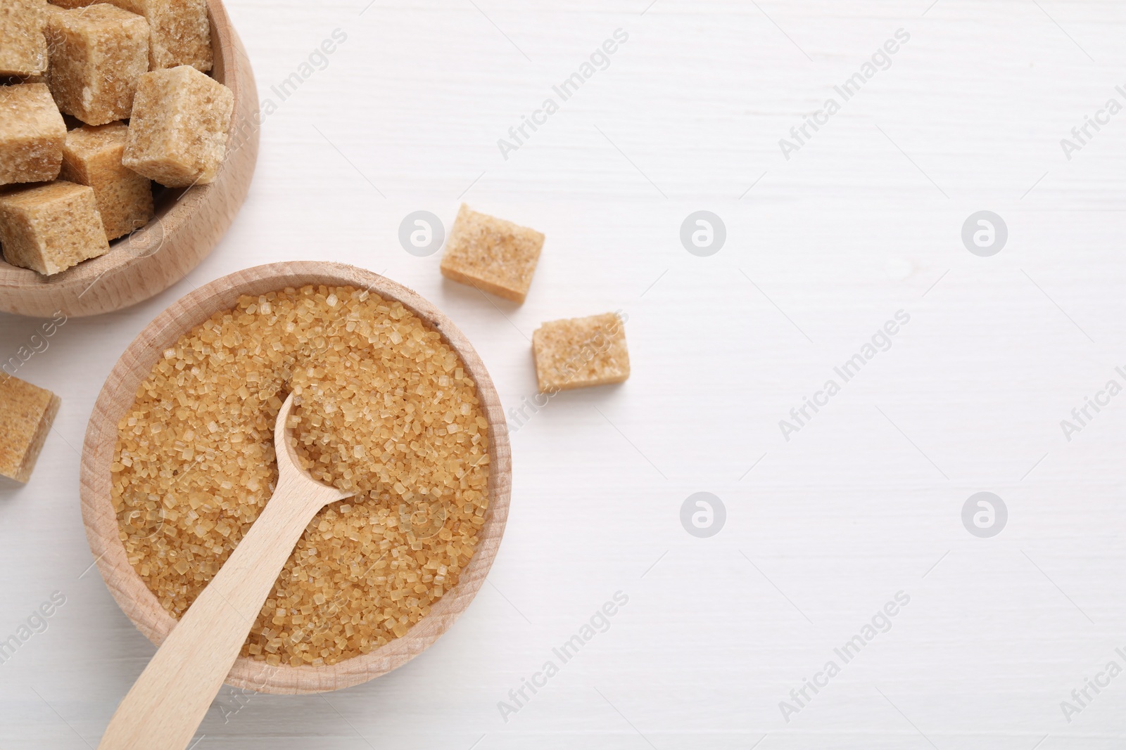 Photo of Bowls and spoon with different types of brown sugar on white wooden table, flat lay. Space for text