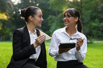 Photo of Happy colleagues having business lunch on green grass in park