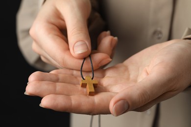 Photo of Woman holding wooden Christian cross on black background, closeup