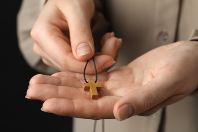 Woman holding wooden Christian cross on black background, closeup