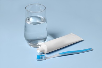Photo of Plastic toothbrush with paste and glass of water on light background