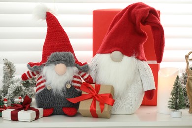 Photo of Funny Christmas gnomes and gift boxes on commode in room with festive decoration