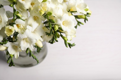 Beautiful freesia flowers in vase on white table, above view