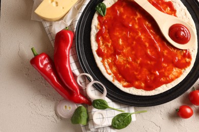 Photo of Pizza base smeared with tomato sauce and products on light textured table, flat lay