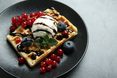 Delicious Belgian waffle with ice cream, berries and chocolate sauce on grey table. Space for text