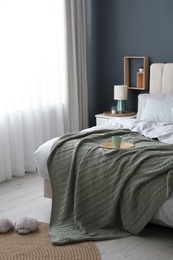 Comfortable bed with knitted green plaid in stylish room interior