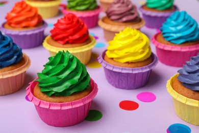 Photo of Many delicious colorful cupcakes and confetti on violet background, closeup