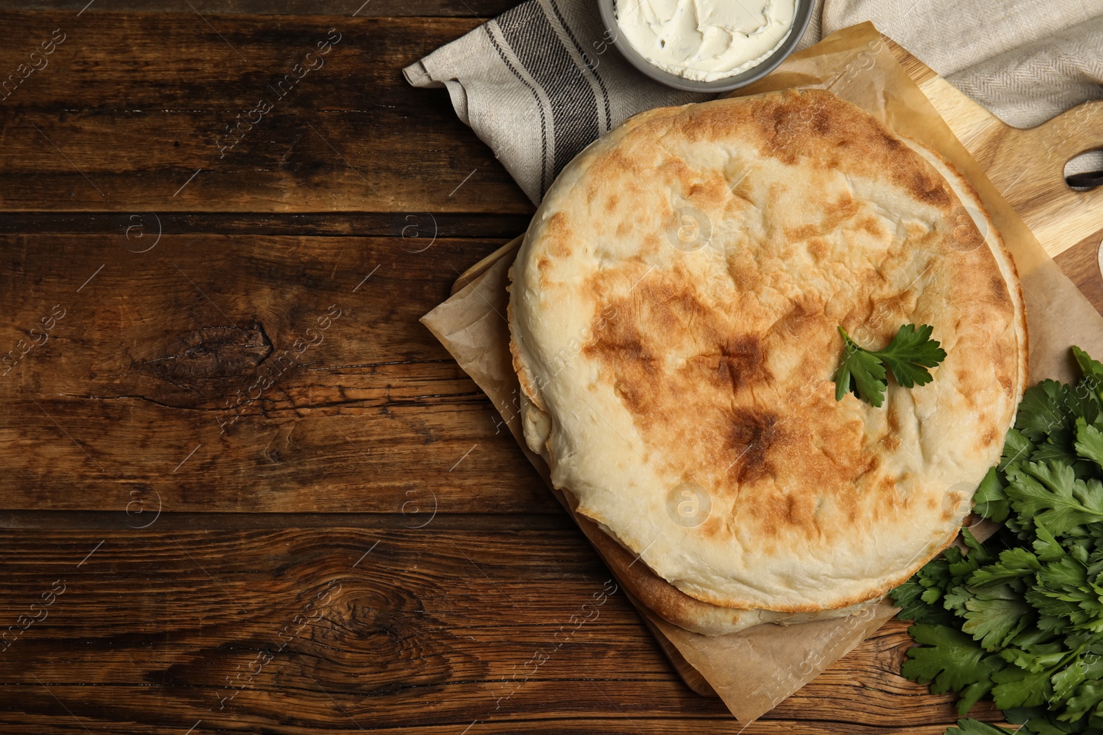 Photo of Loaves of delicious homemade pita bread, cream cheese and parsley on wooden table, flat lay. Space for text