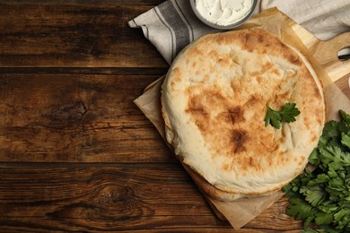 Photo of Loaves of delicious homemade pita bread, cream cheese and parsley on wooden table, flat lay. Space for text