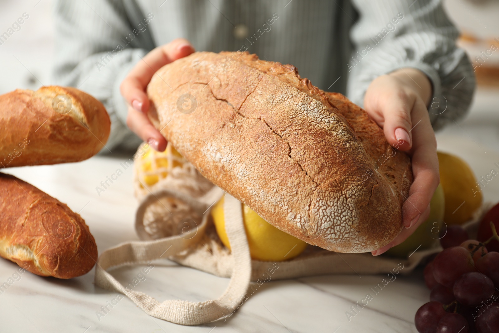 Photo of Woman bread and string bag of fresh fruits at light marble table, closeup