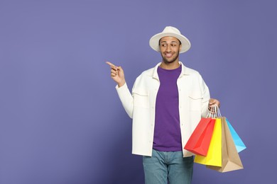 Photo of Happy African American man in hat with shopping bags on purple background. Space for text