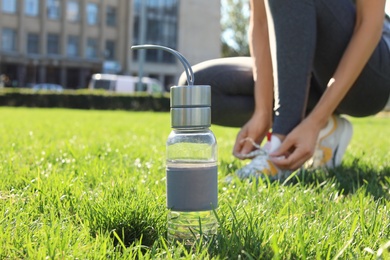 Photo of Bottle with water near woman lacing her sneakers outdoors