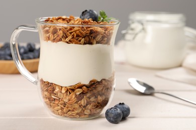 Tasty yogurt with muesli and blueberries in glass cup served on white wooden table