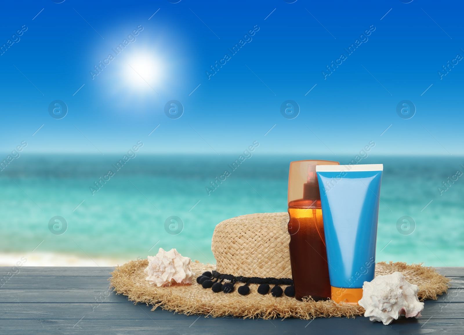 Image of Skin sun protection products and hat on blue wooden table against seascape. Space for design