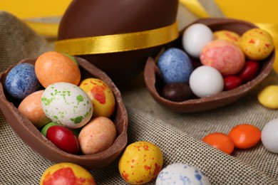 Whole and halves of chocolate eggs with colorful candies on cloth, closeup